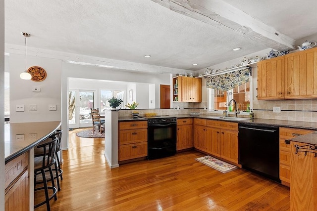 kitchen with a peninsula, a sink, light wood-style floors, black appliances, and dark countertops