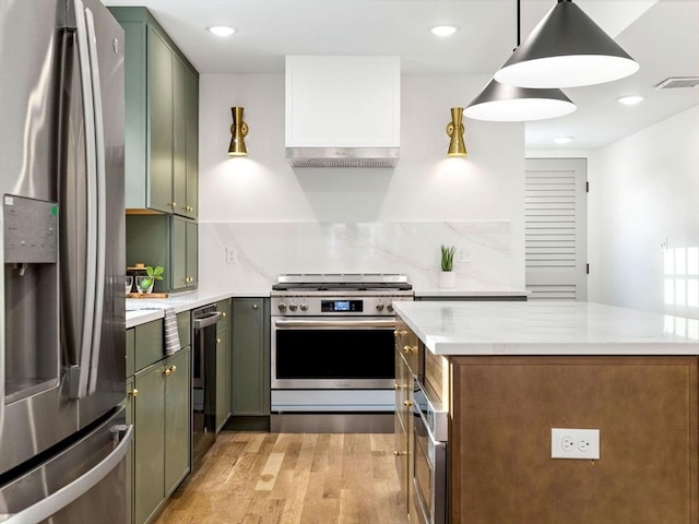 kitchen with appliances with stainless steel finishes, decorative light fixtures, light stone countertops, light wood-type flooring, and green cabinetry