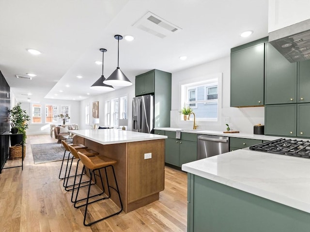 kitchen featuring a center island, green cabinetry, appliances with stainless steel finishes, decorative light fixtures, and light stone counters