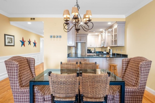 dining room featuring sink, ornamental molding, light wood-type flooring, and an inviting chandelier