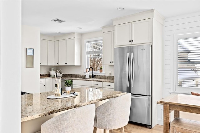 kitchen featuring sink, stainless steel refrigerator, a kitchen breakfast bar, light stone counters, and white cabinets