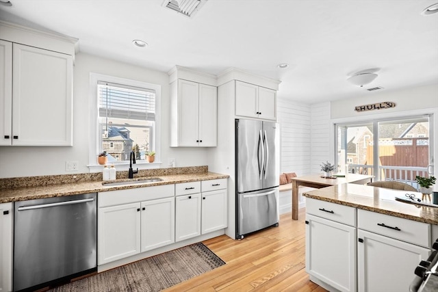 kitchen with stone counters, white cabinetry, sink, stainless steel appliances, and light wood-type flooring