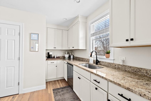 kitchen with sink, dishwasher, light stone countertops, white cabinets, and light wood-type flooring