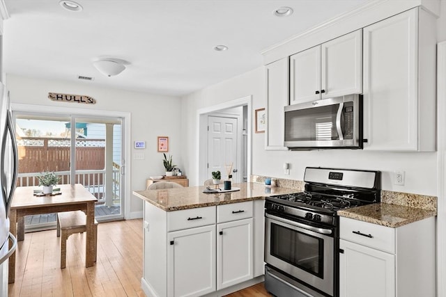 kitchen featuring light hardwood / wood-style flooring, appliances with stainless steel finishes, dark stone countertops, white cabinets, and kitchen peninsula