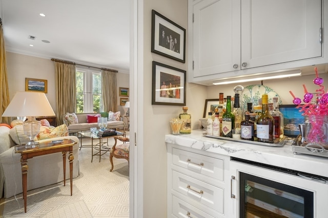 bar with white cabinetry, crown molding, light stone countertops, and beverage cooler