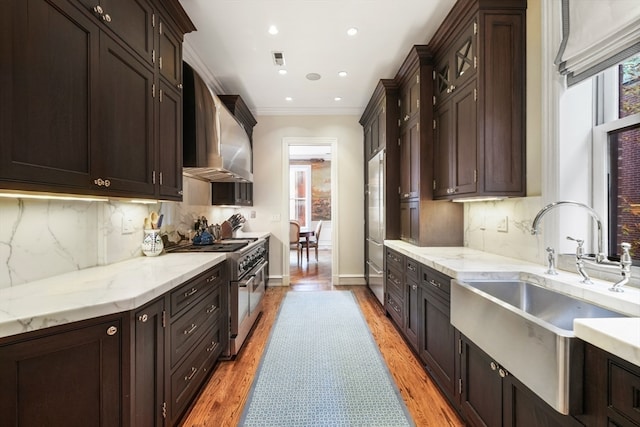 kitchen with backsplash, light hardwood / wood-style floors, wall chimney exhaust hood, high end stove, and ornamental molding