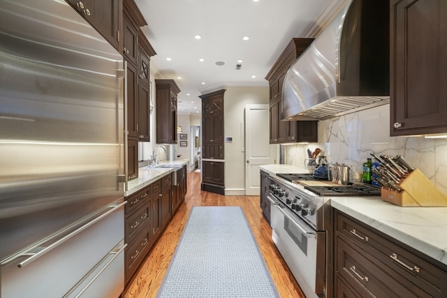 kitchen featuring high quality appliances, crown molding, wall chimney range hood, and light wood-type flooring