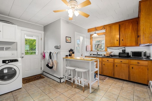 kitchen with washer / clothes dryer, stainless steel microwave, baseboard heating, brown cabinets, and ornamental molding
