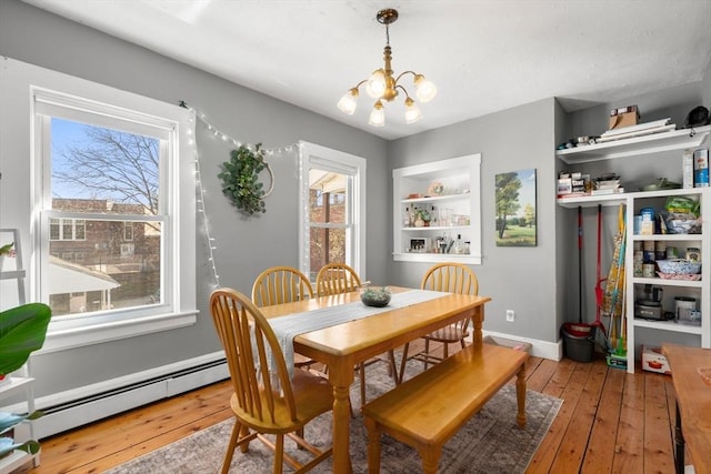 dining room featuring a chandelier, a baseboard radiator, wood-type flooring, and baseboards