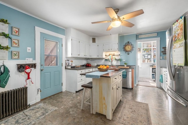 kitchen featuring radiator, appliances with stainless steel finishes, tasteful backsplash, a ceiling fan, and a center island