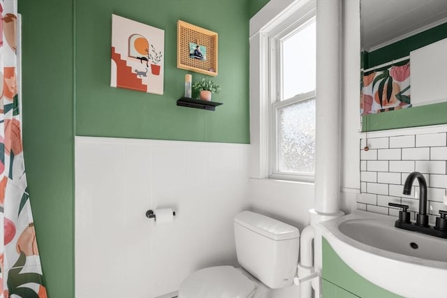 bathroom with toilet, decorative backsplash, vanity, a wainscoted wall, and curtained shower