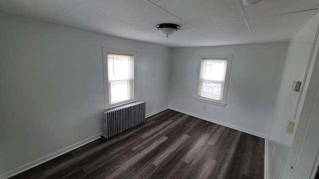 unfurnished room featuring radiator heating unit, plenty of natural light, dark wood-style floors, and baseboards