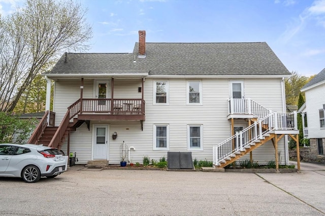 rear view of property featuring stairs, a chimney, and a shingled roof