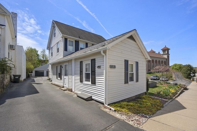 view of property exterior featuring a detached garage, a shingled roof, and an outbuilding
