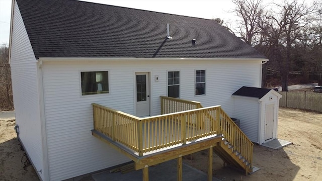 back of property featuring a deck, an outdoor structure, fence, and roof with shingles