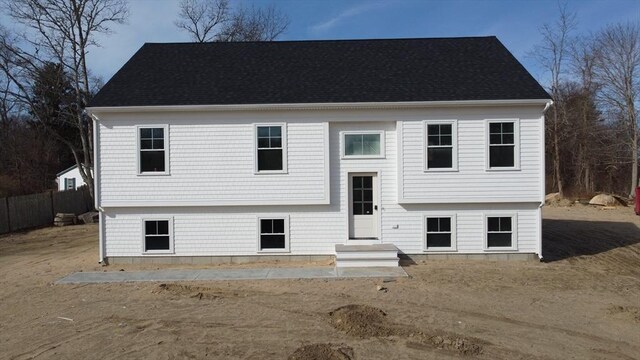 bi-level home featuring a shingled roof and fence