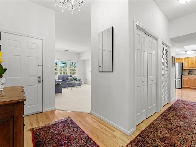 hallway featuring baseboards, light wood finished floors, and a chandelier