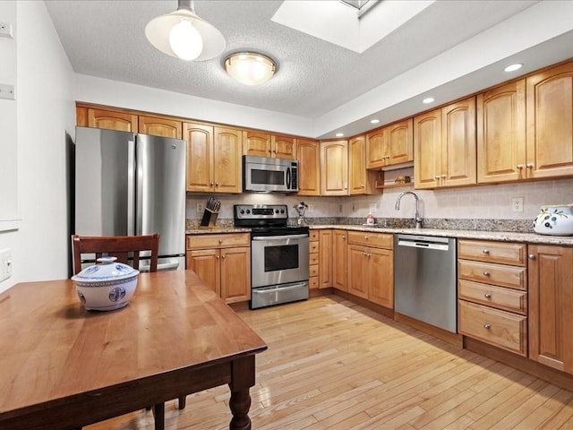 kitchen with light wood finished floors, appliances with stainless steel finishes, a skylight, and a sink