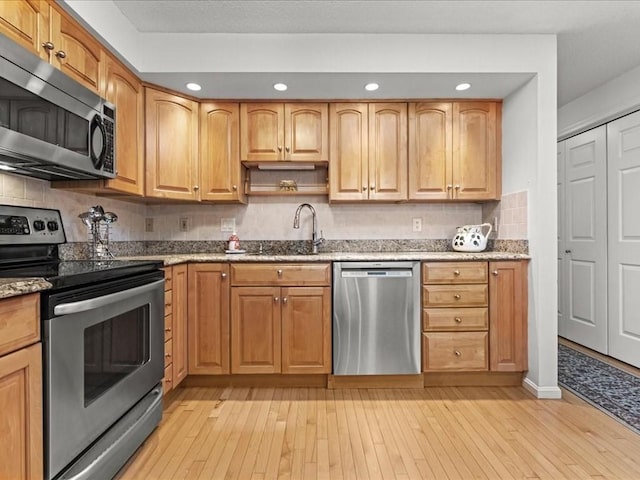 kitchen featuring tasteful backsplash, light stone countertops, light wood-style floors, stainless steel appliances, and a sink