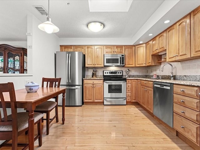 kitchen featuring visible vents, light stone counters, light wood-style floors, stainless steel appliances, and a sink