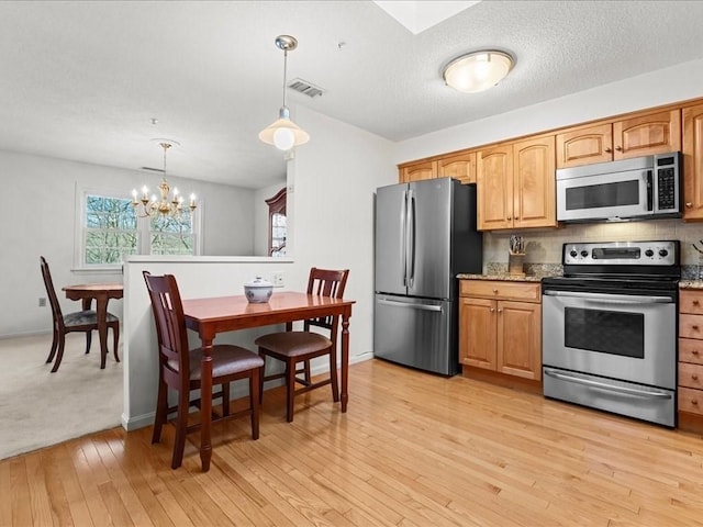 kitchen with visible vents, tasteful backsplash, light wood-style floors, appliances with stainless steel finishes, and hanging light fixtures