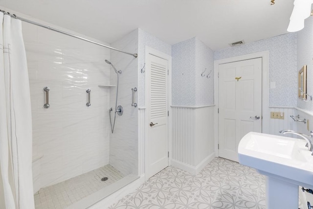 bathroom with tile patterned flooring, a wainscoted wall, tiled shower, visible vents, and a sink