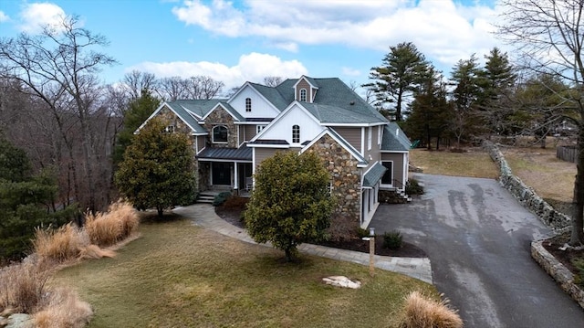 view of front of house with aphalt driveway, stone siding, and a front lawn