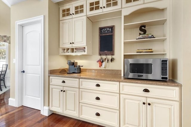 kitchen with glass insert cabinets, stainless steel microwave, open shelves, and dark wood-type flooring