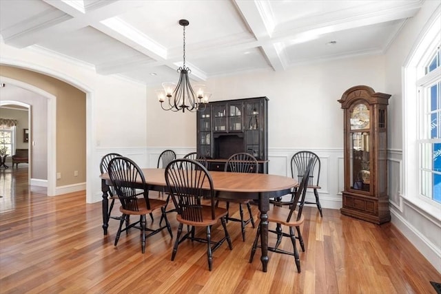 dining area featuring arched walkways, coffered ceiling, light wood-type flooring, beam ceiling, and an inviting chandelier