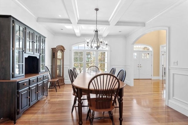 dining room with a chandelier, beam ceiling, a decorative wall, and light wood finished floors