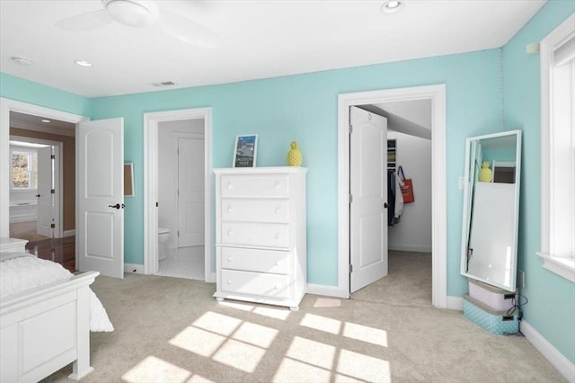 bedroom featuring baseboards, visible vents, light colored carpet, ensuite bath, and a walk in closet