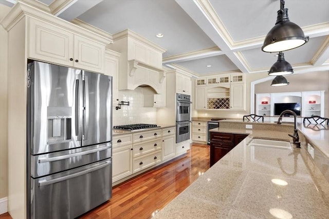 kitchen featuring stainless steel appliances, coffered ceiling, a sink, light wood-style floors, and hanging light fixtures