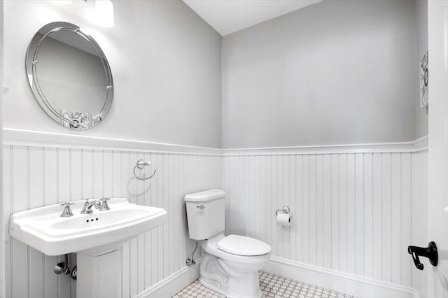 bathroom with toilet, tile patterned floors, a sink, and wainscoting