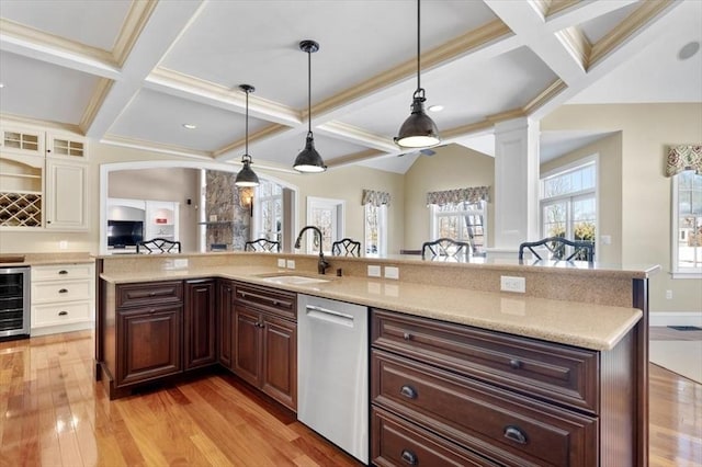 kitchen with light wood finished floors, decorative columns, beam ceiling, stainless steel dishwasher, and a sink