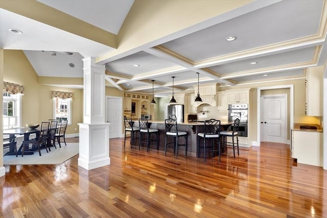 kitchen featuring appliances with stainless steel finishes, a breakfast bar area, wood finished floors, and ornate columns