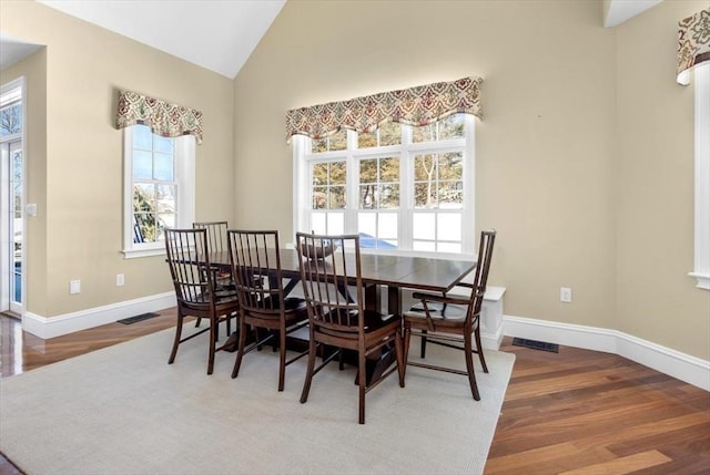 dining room featuring baseboards, visible vents, vaulted ceiling, and wood finished floors