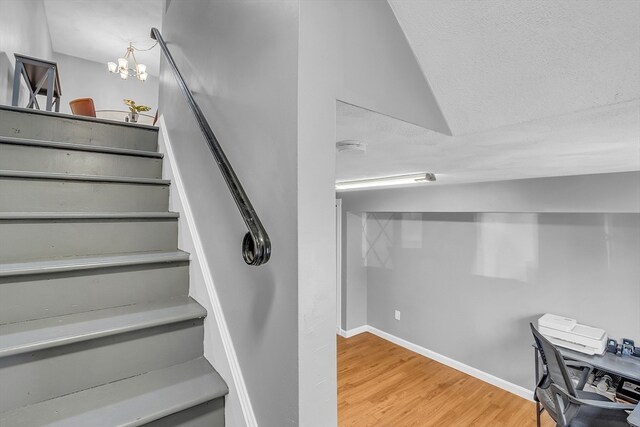 staircase with wood-type flooring and an inviting chandelier