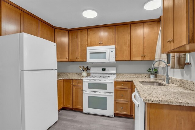 kitchen featuring light stone countertops, light wood-type flooring, white appliances, and sink