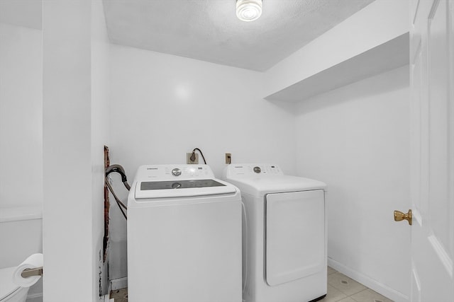 laundry area with washing machine and dryer, light tile patterned floors, and a textured ceiling