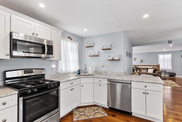 kitchen with white cabinets, dark wood-style floors, appliances with stainless steel finishes, a peninsula, and a sink