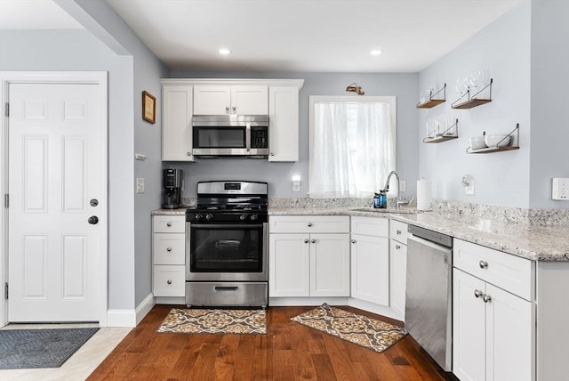 kitchen with light stone counters, dark wood-style flooring, appliances with stainless steel finishes, white cabinetry, and a sink