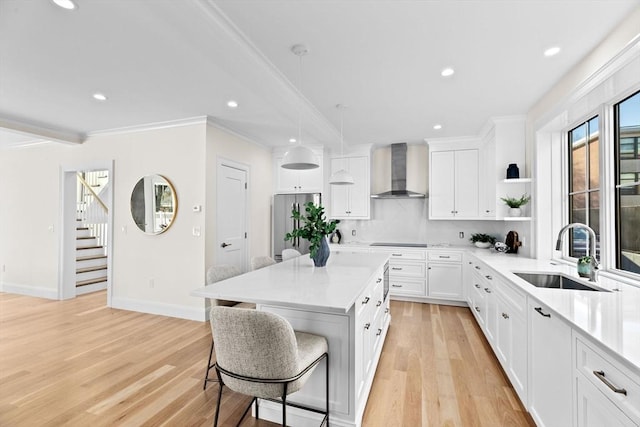 kitchen with stainless steel refrigerator, sink, wall chimney range hood, pendant lighting, and white cabinets