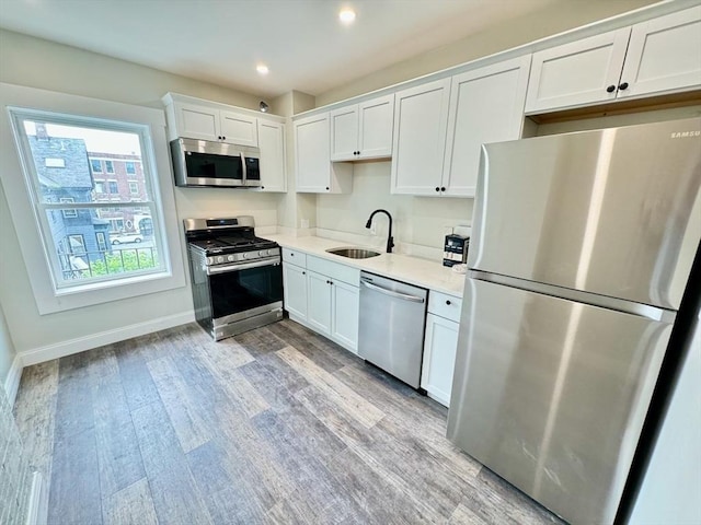 kitchen with sink, light wood-type flooring, white cabinetry, light stone counters, and stainless steel appliances