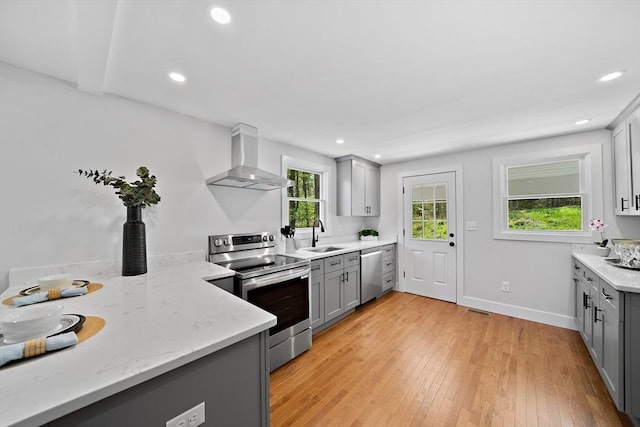 kitchen featuring light hardwood / wood-style flooring, appliances with stainless steel finishes, wall chimney exhaust hood, sink, and gray cabinetry