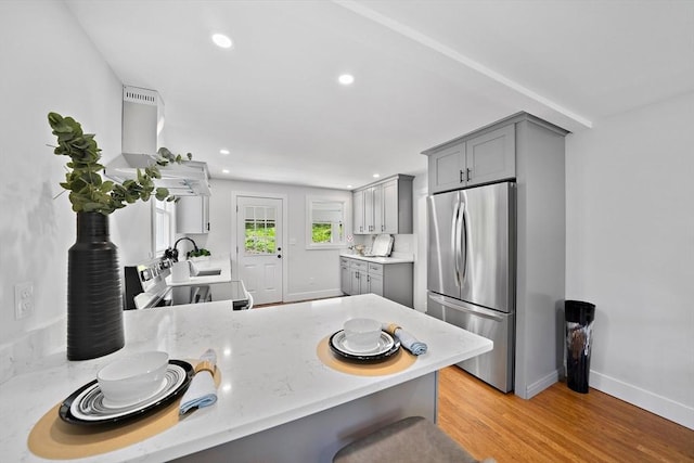 kitchen featuring range hood, kitchen peninsula, appliances with stainless steel finishes, and gray cabinetry