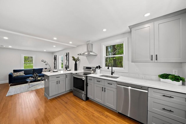 kitchen with kitchen peninsula, appliances with stainless steel finishes, wall chimney exhaust hood, sink, and gray cabinetry