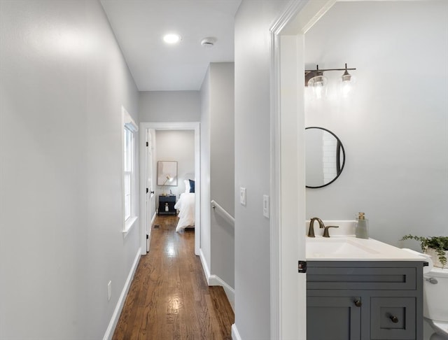 hall with dark wood-type flooring, a sink, and baseboards