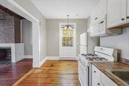 kitchen featuring white appliances, hardwood / wood-style flooring, white cabinetry, a notable chandelier, and decorative light fixtures