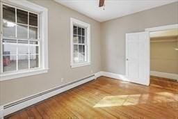 empty room featuring wood-type flooring, a baseboard heating unit, and ceiling fan