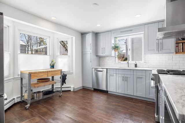 kitchen with wall chimney range hood, stainless steel appliances, a sink, and gray cabinetry